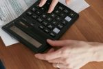 Person calculating finances with a calculator and document on a wooden desk.